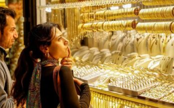 A conceptual financial image showing physical gold bars and coins stacked against a downward red stock market arrow, representing the sudden drop in the Gold price today.