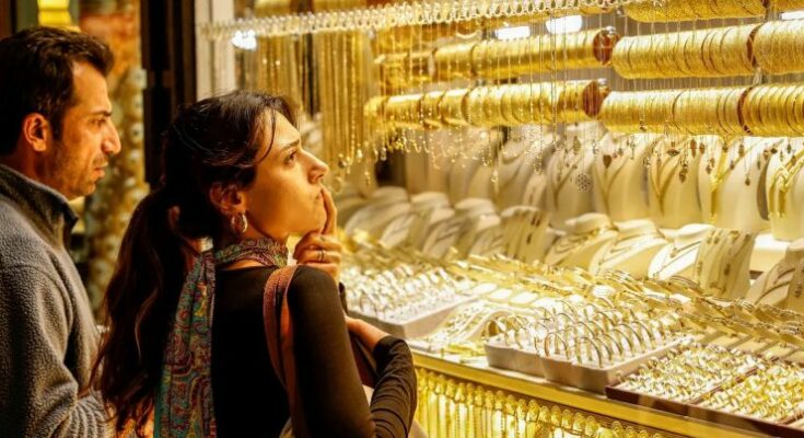 A conceptual financial image showing physical gold bars and coins stacked against a downward red stock market arrow, representing the sudden drop in the Gold price today.