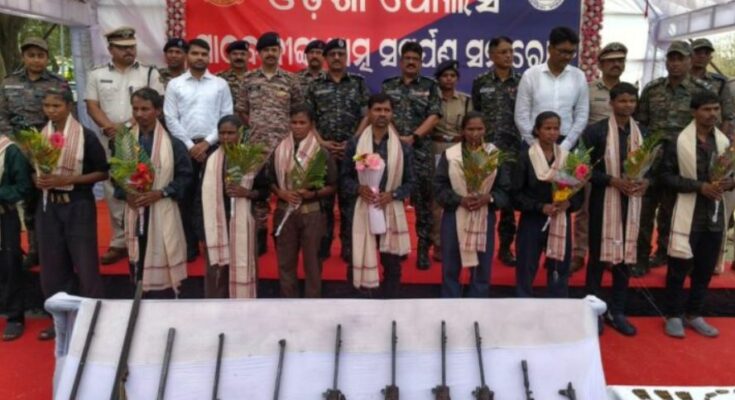 Surrendered Maoists laying down their arms before the Odisha Police and CRPF officials, signifying a major success in anti-Naxal operations.