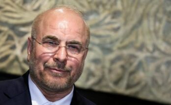 ईरानी सैन्य अधिकारी और बैकग्राउंड में अमेरिकी झंडे के साथ जंगी जहाज का प्रतीकात्मक चित्र