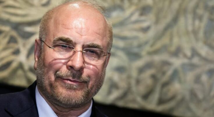 ईरानी सैन्य अधिकारी और बैकग्राउंड में अमेरिकी झंडे के साथ जंगी जहाज का प्रतीकात्मक चित्र