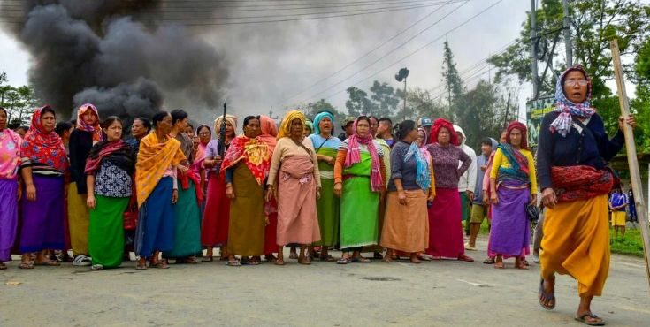 A conceptual image highlighting the Manipur Violence Updates, showing heavily armed CRPF personnel patrolling a smoke-filled street in Bishnupur, with a crossed-out Wi-Fi symbol representing the internet suspension.
